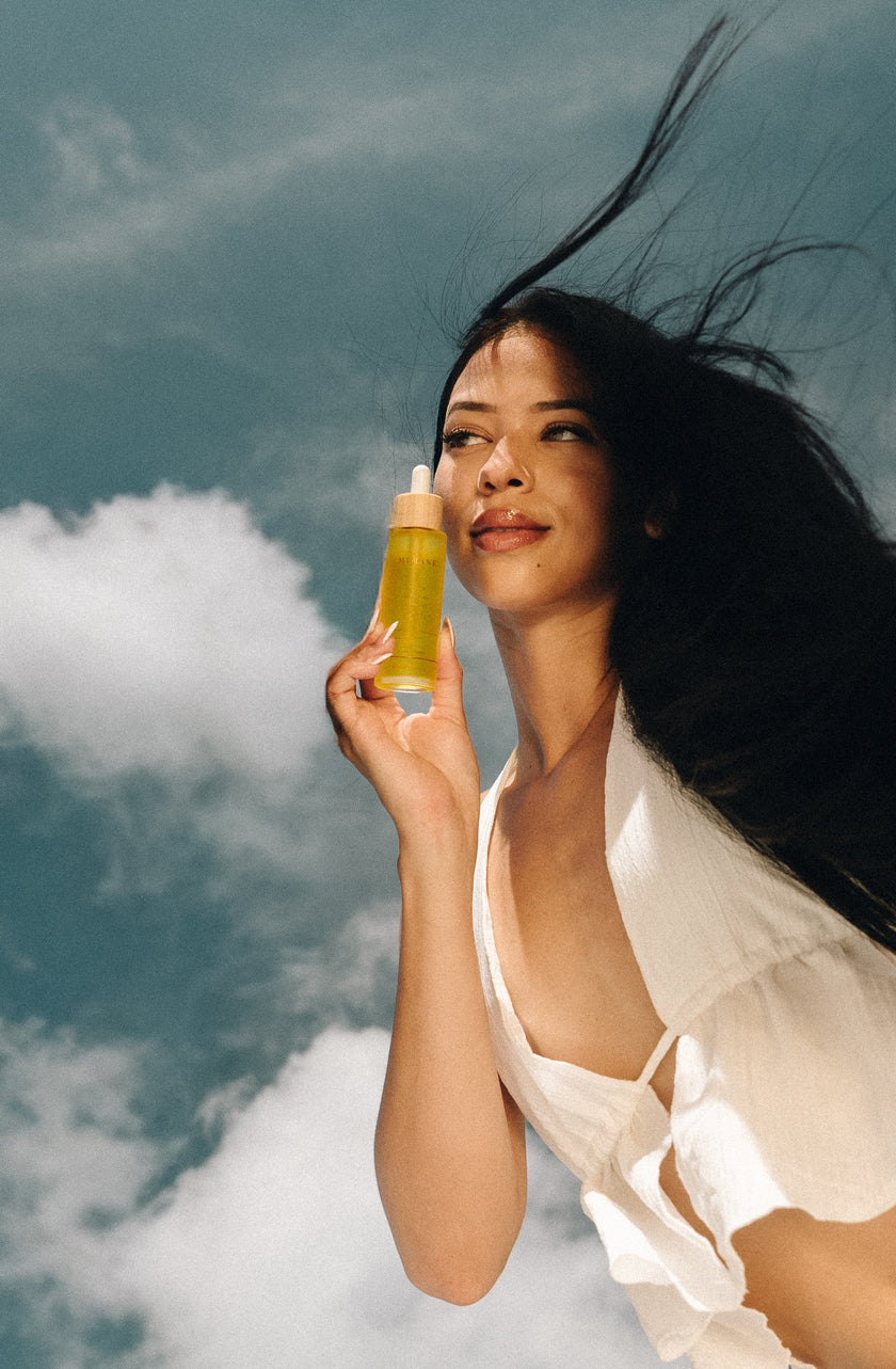 Woman holding the Mimane Glow Growth & Strengthen Hair Oil against a blue sky