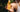 Close-up of a hand holding the Mimane Glow hair oil dropper bottle against palm leaves