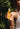 Close-up of a hand holding the Mimane Glow hair oil dropper bottle against palm leaves