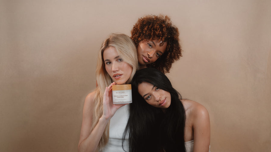 Three models leaning together in a studio, the Hydrate and Strengthen Hair Mask jar in hand, launch hero