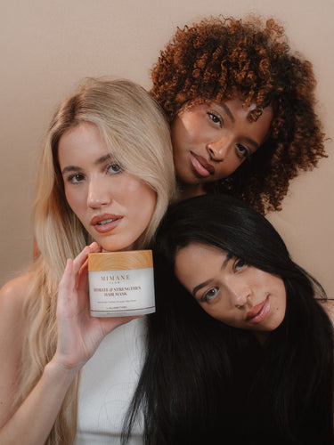 Three models leaning together in a studio, the Hydrate and Strengthen Hair Mask jar in hand, launch hero for mobile