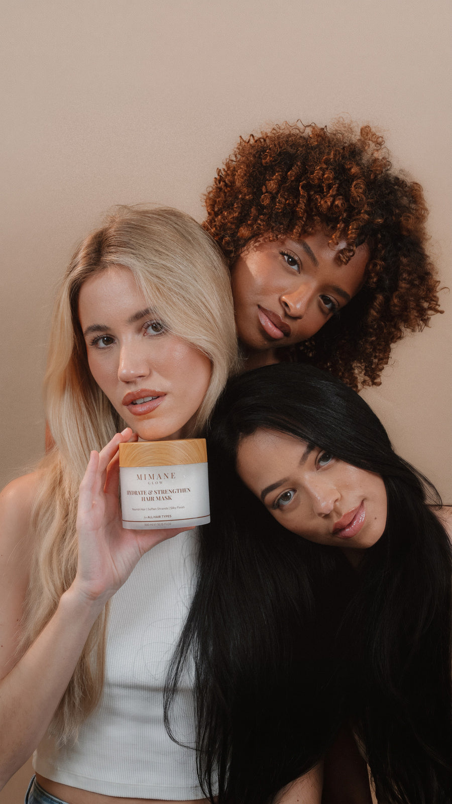 Three models leaning together in a studio, the Hydrate and Strengthen Hair Mask jar in hand, launch hero for mobile